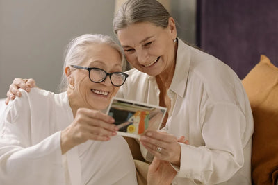 Two elderly women sharing a nostalgic moment looking at a physical photo, illustrating the joy of digitizing memories onto a Picrora frame.