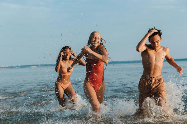 Young friends running and splashing in the water at the beach, showing the dynamic travel photos you can display on a Picrora screen.