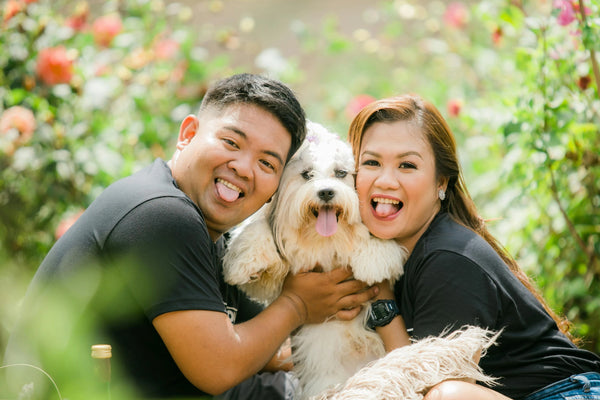 Happy couple holding their white dog outdoors, capturing a precious family moment to share on a Picrora smart frame.