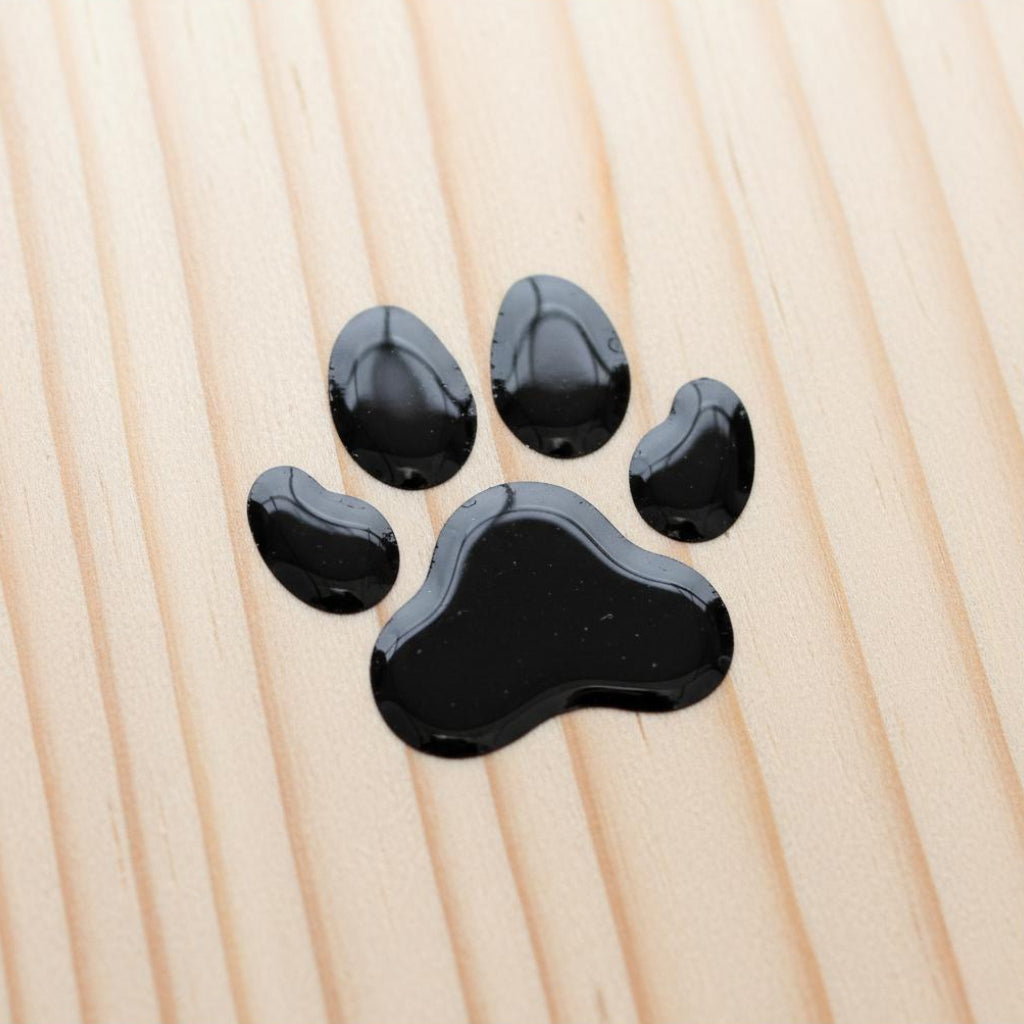 Glossy black paw print UV decal applied to a light pine wood surface for personalized pet gifts.