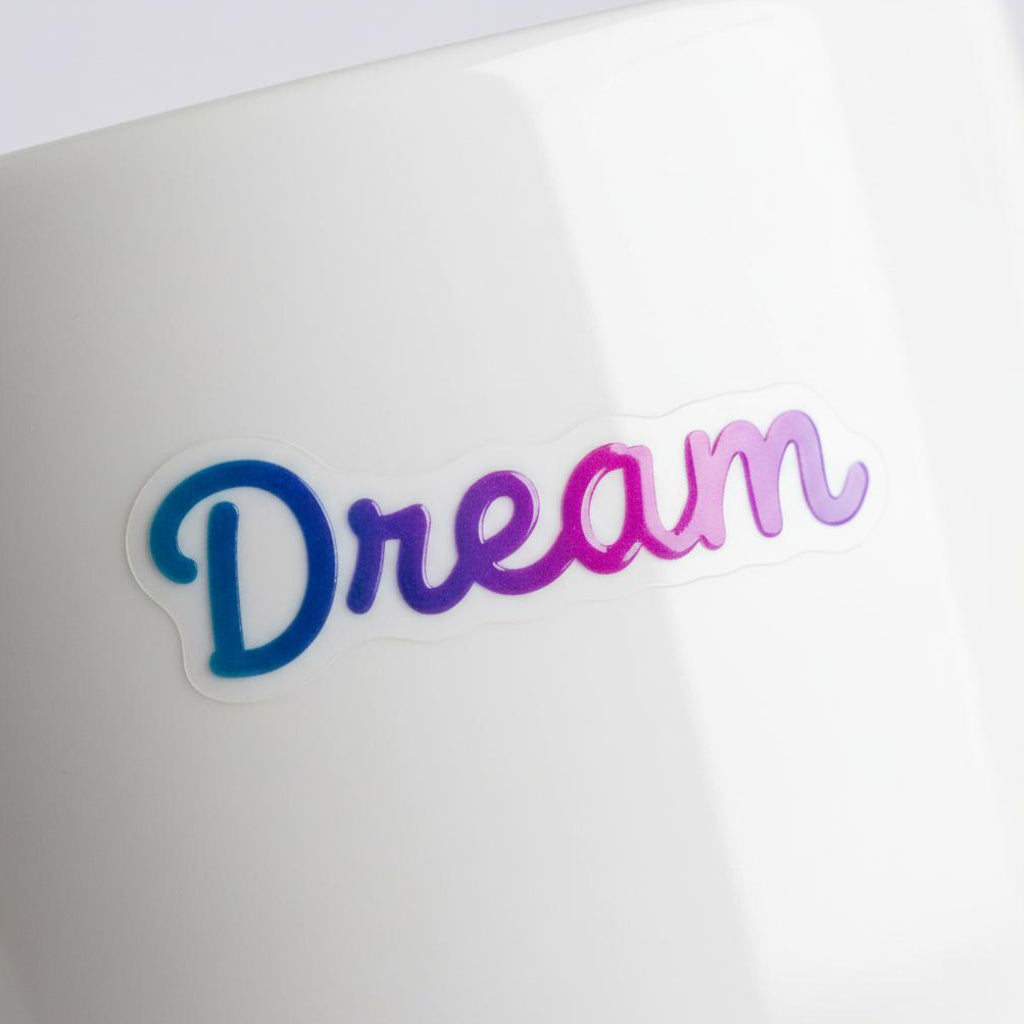 Blue and purple gradient UV transfer decal reading Dream applied to a white ceramic mug surface.